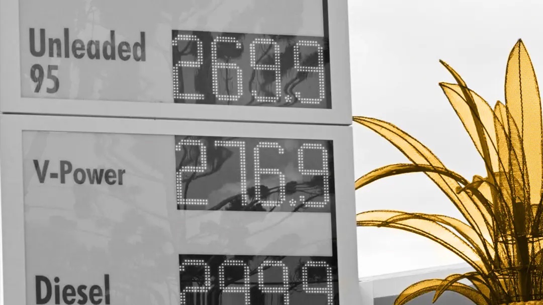 Petrol station price board showing fuel costs beside a large decorative pineapple sculpture. 