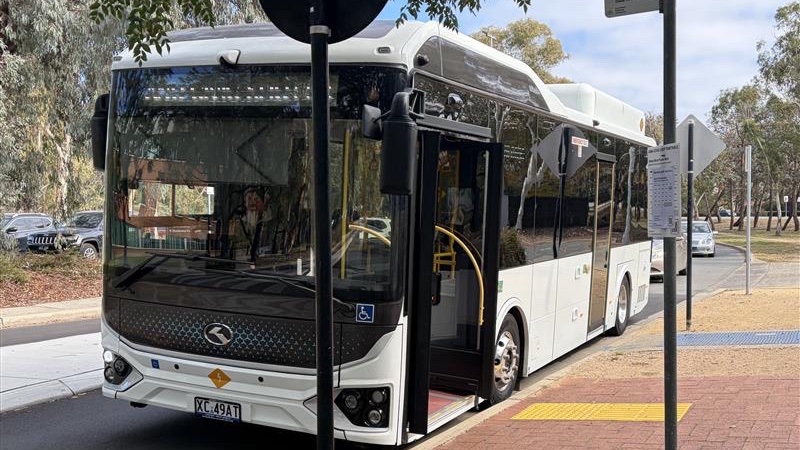 A parked white bus with ANU Civic loop reflecting on the front.