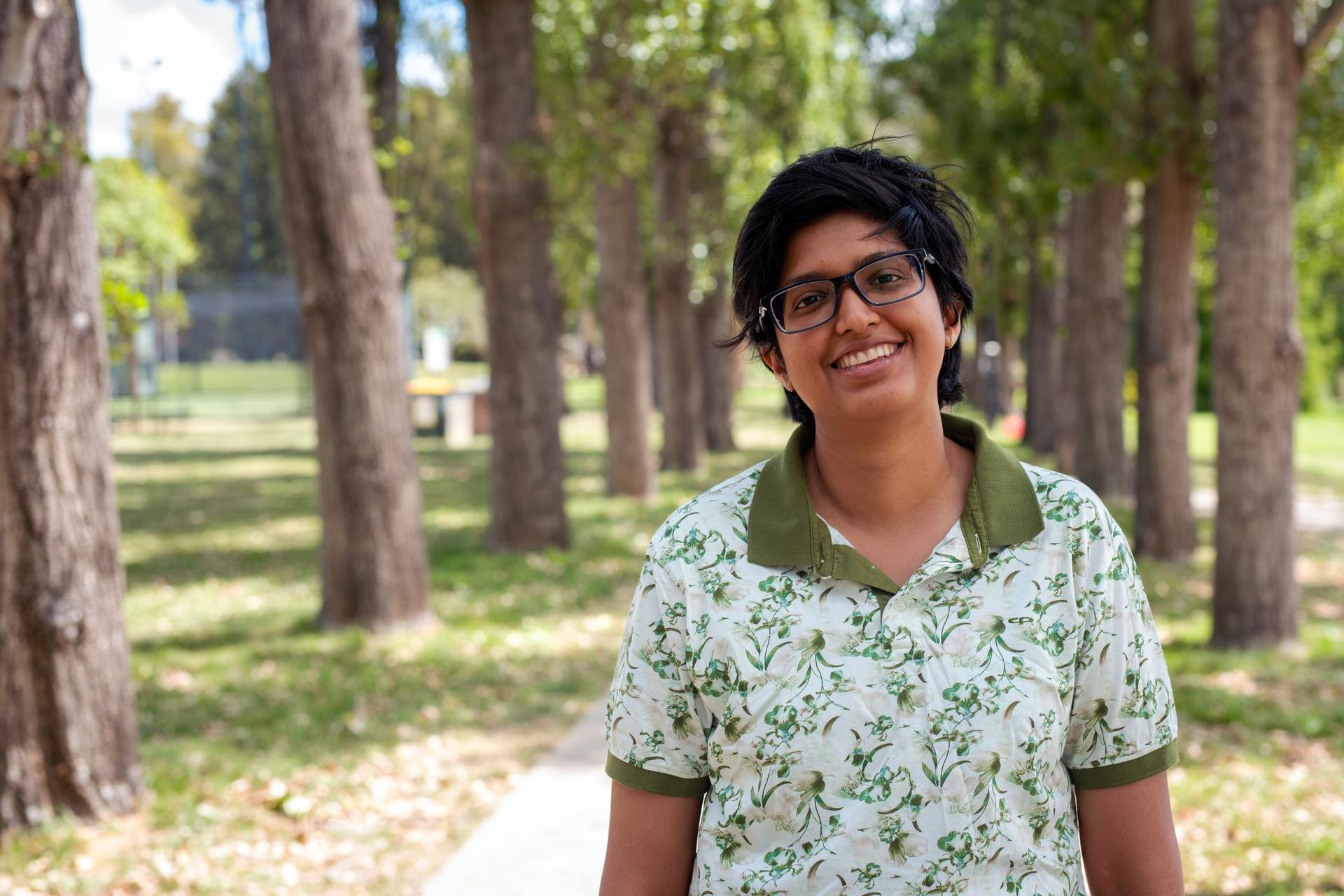 Lakshmi Raja smiling at camera on a tree-lined path in a park.