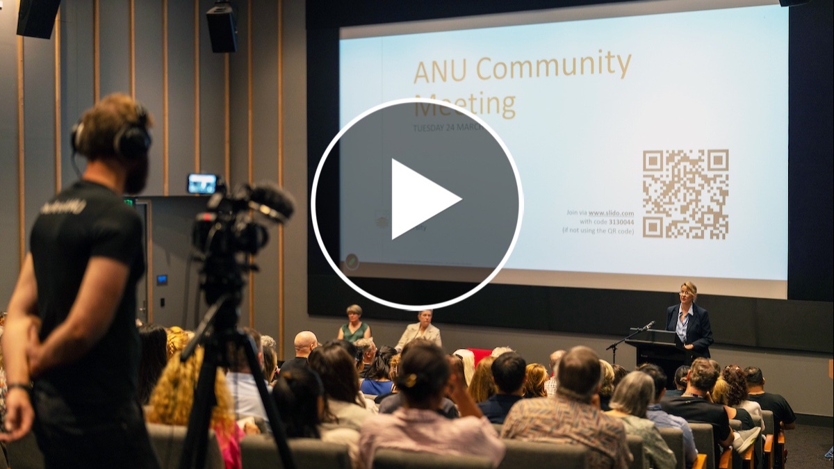 Audience watching a speaker at an ANU Community Meeting presentation in a lecture theatre, with a camera operator filming. 
