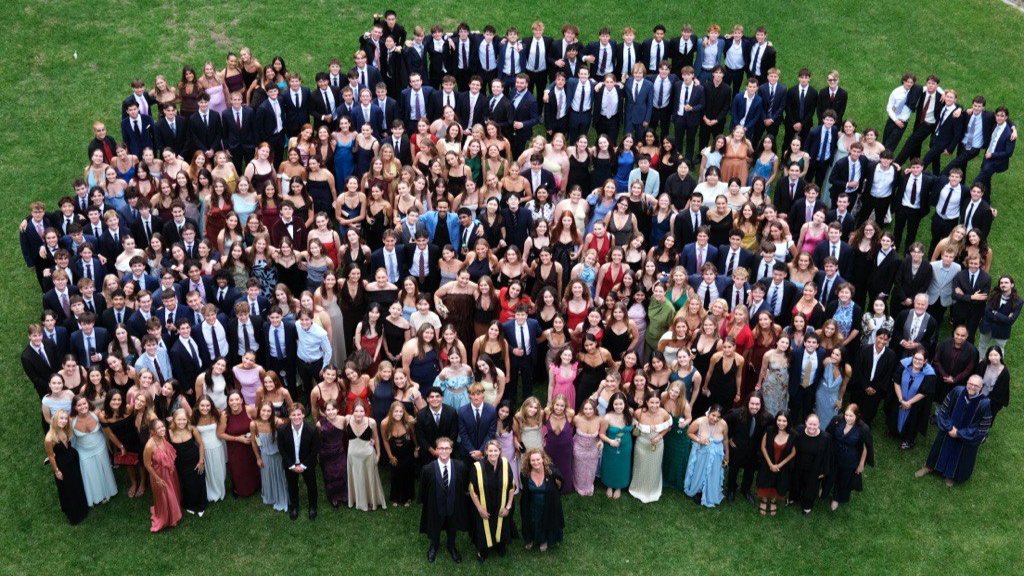 Large group of formally dressed people gathered outdoors on a lawn, posing for a group photo.