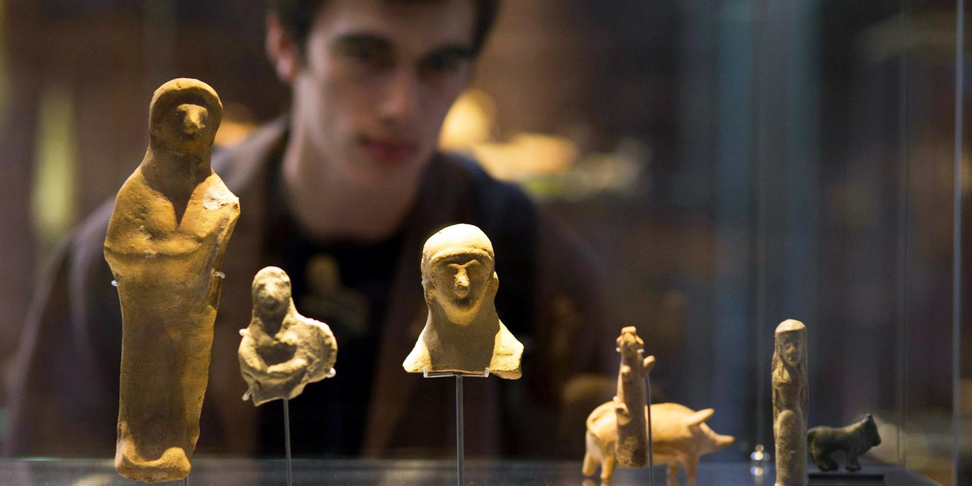 Ancient figurines displayed in a glass case, with a person observing them in the background.