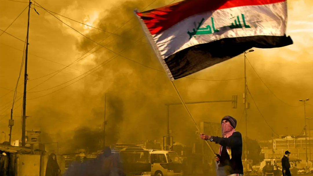 Person waving an Iraqi flag amid smoke during a street protest in the Middle East.