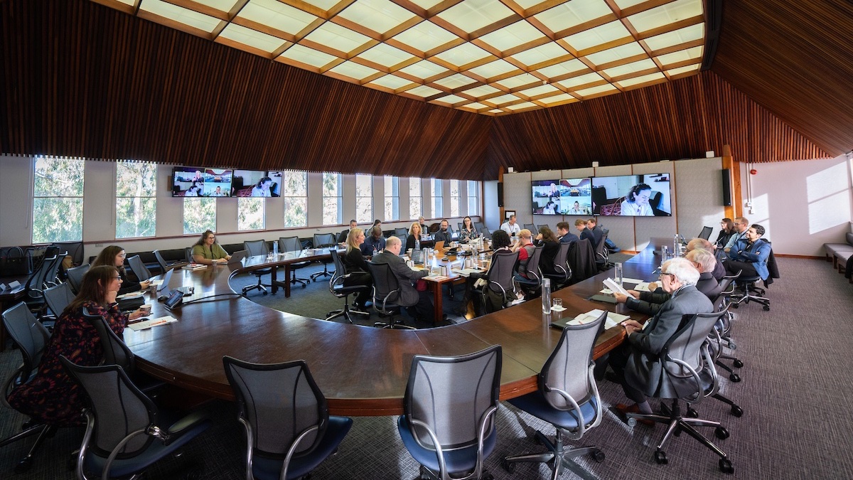  A group of people sitting around a conference table and another small group of people sitting at the circumventing conference table 