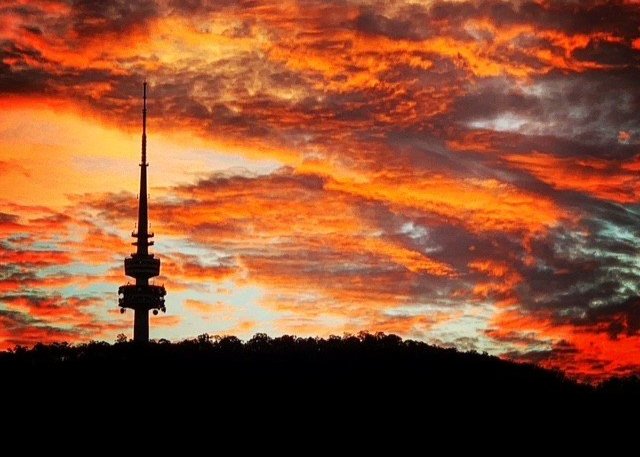 Silhouette of Telstra Tower on Black Mountain against dramatic orange clouds at dusk.