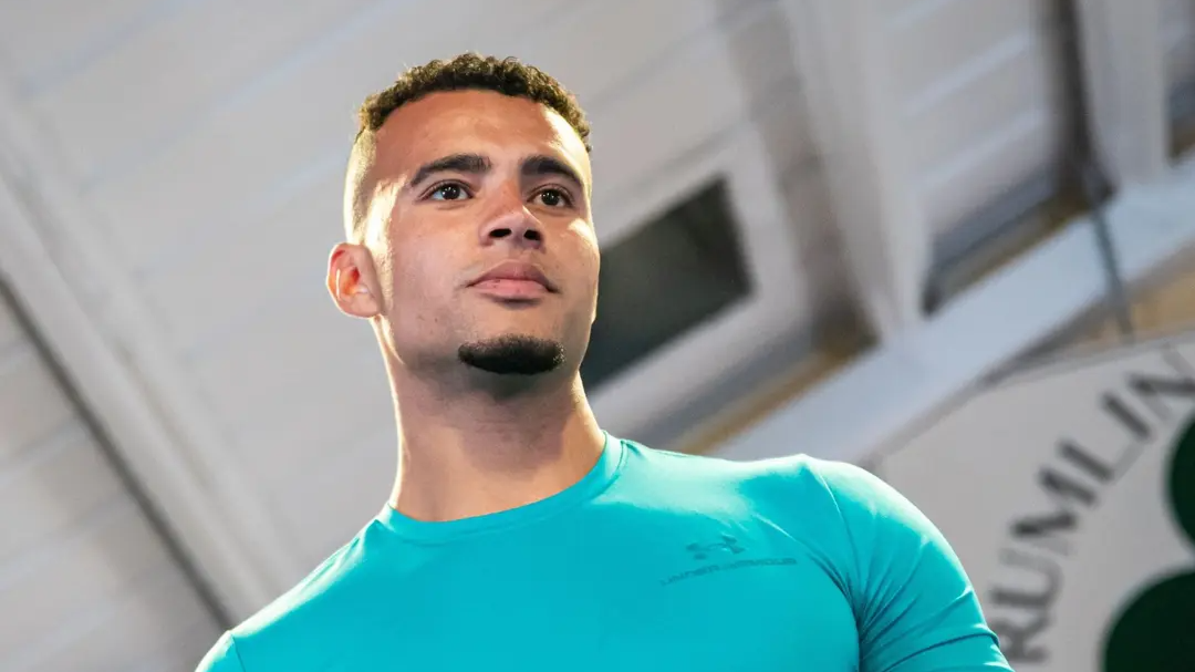 Low-angle portrait of a man in a teal athletic shirt looking ahead in an indoor setting.