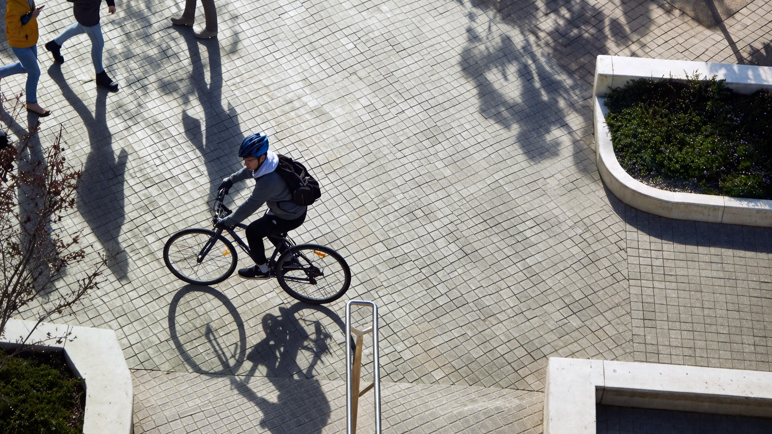 Overhead view of a cyclist riding across a paved campus courtyard with pedestrians nearby.