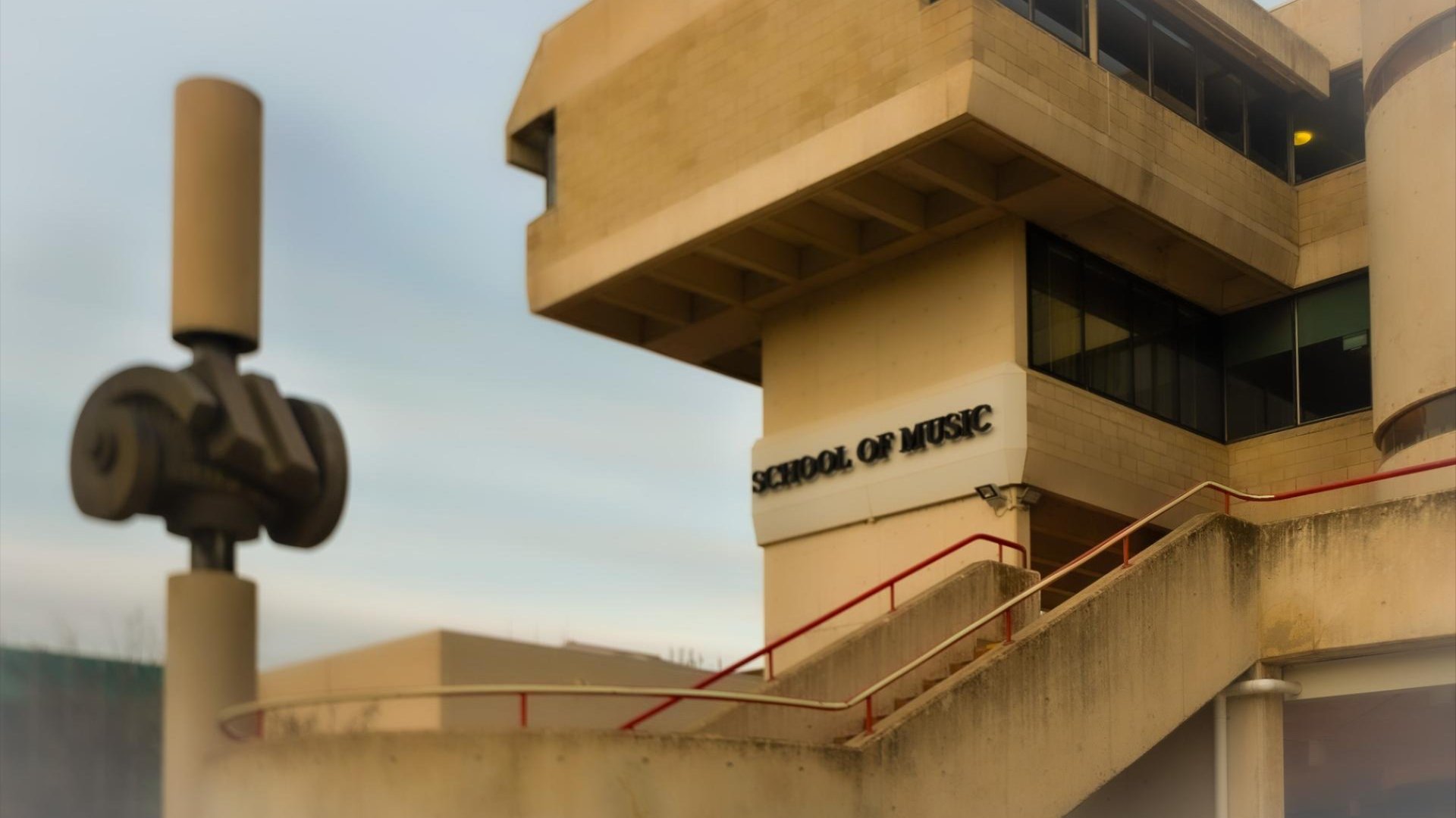 Exterior of the ��������School of Music building with concrete staircases and signage in soft evening light.
