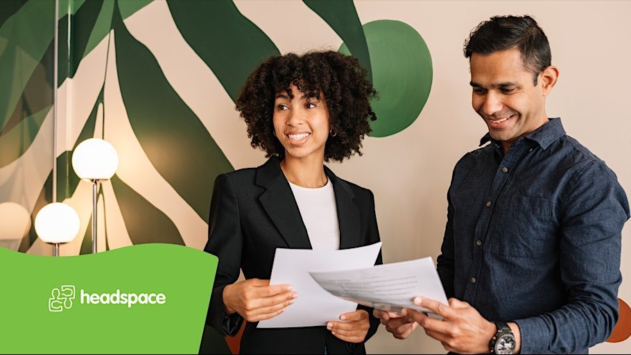 Two colleagues review documents together and smile, with the Headspace logo visible in the corner.