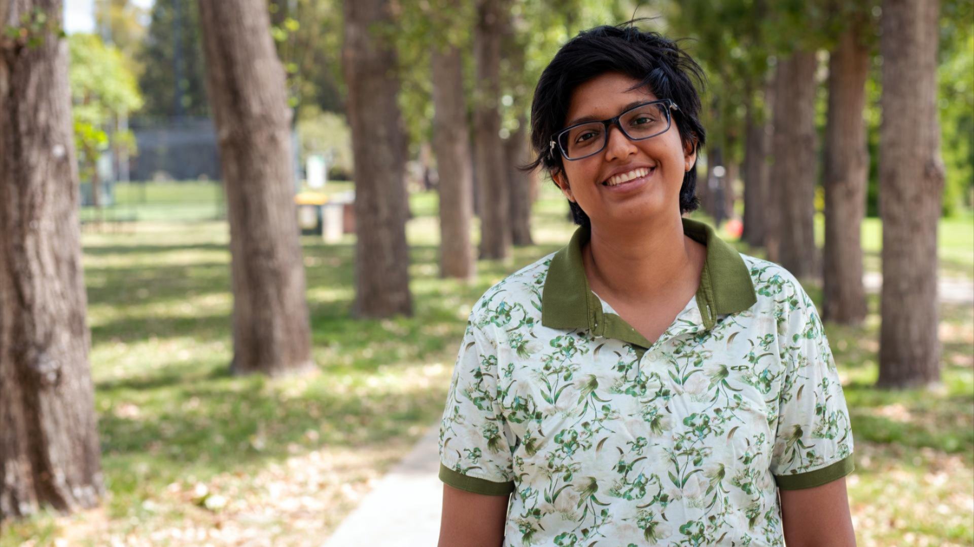Person smiling at camera on a tree-lined path in a park.