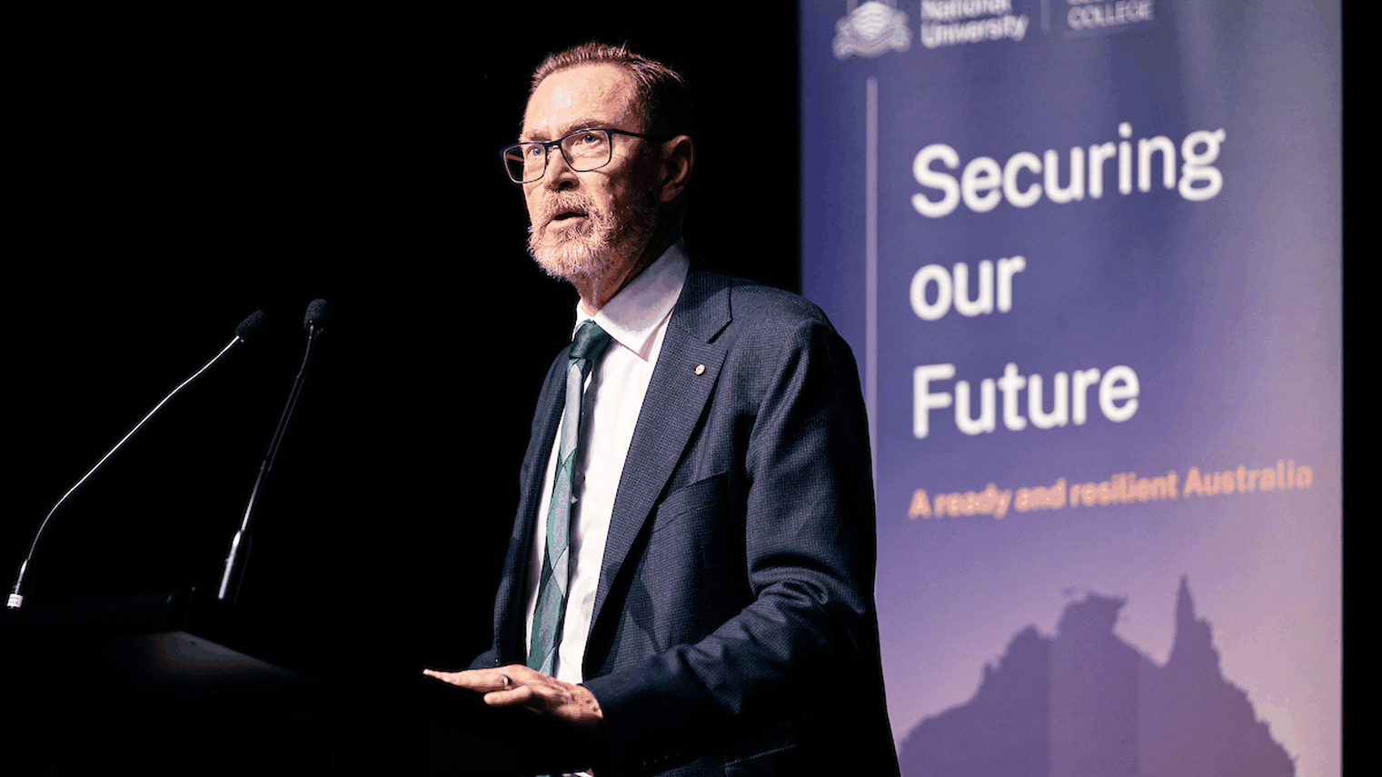 Group of speakers seated on stage in armchairs, one man speaking into a microphone during a panel discussion.