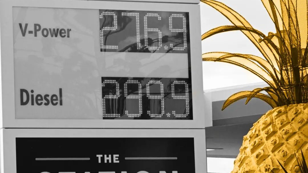 Petrol station price board showing fuel costs beside a large decorative pineapple sculpture.