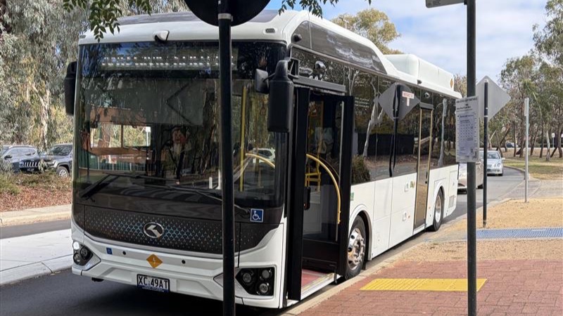 A parked white bus with ANU Civic loop reflecting on the front.