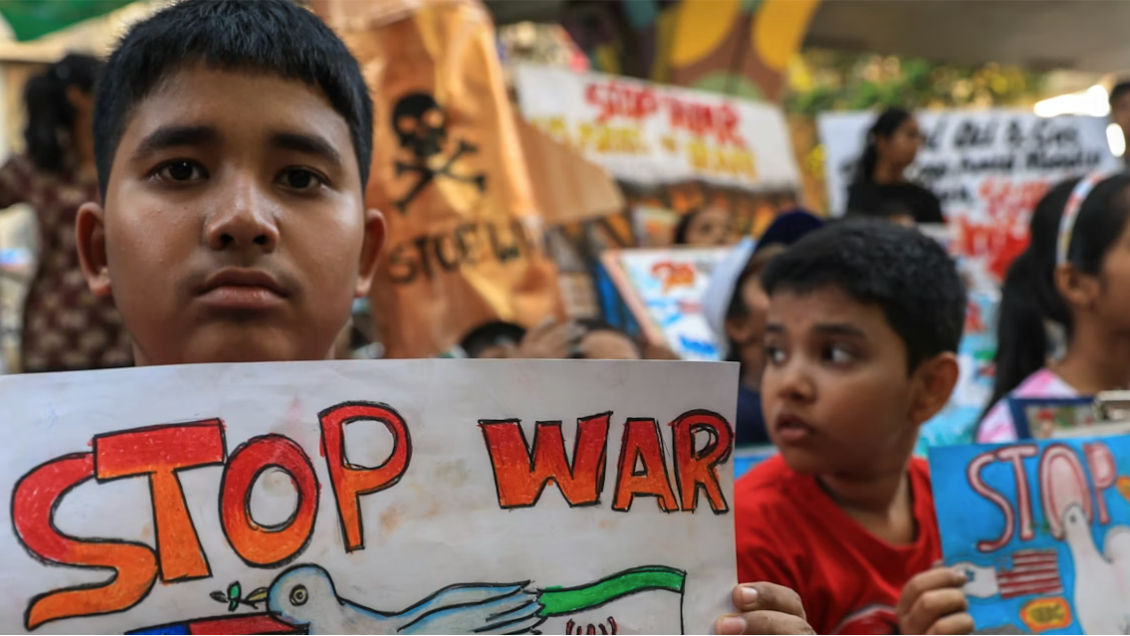 Children holding &ldquo;Stop war&rdquo; signs at a protest, with other children and banners visible in the background.