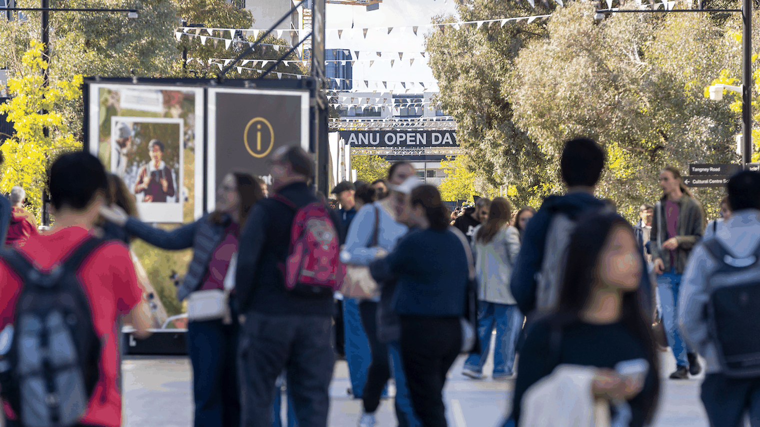 Crowds watch and film the Artemis II rocket launch as it lifts off and arcs through a clear blue sky, leaving a bright smoke trail.