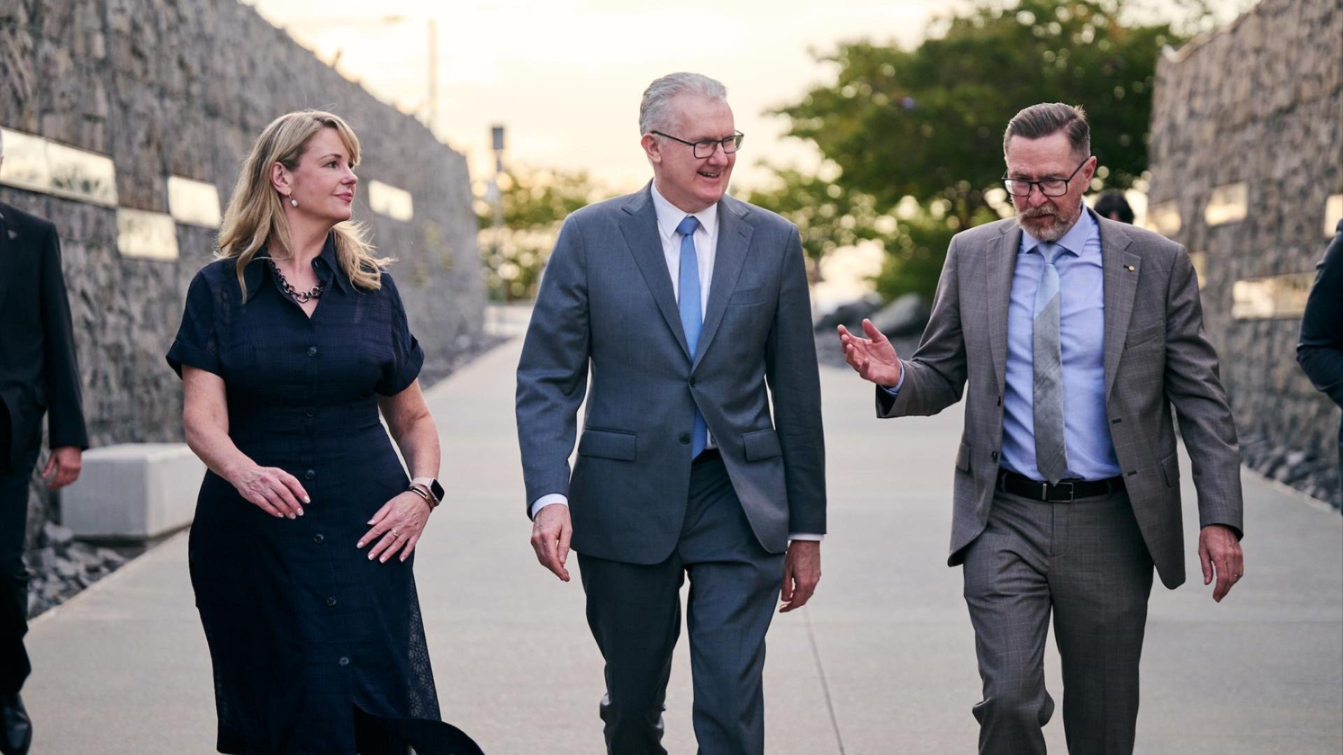 Professor Rebekah Brown, the Hon Tony Burke MP, and Professor Rory Medcalf walk side by side along a brick entryway at the National Arboretum, engaged in conversation as they arrive for the Securing Our Future conference dinner.