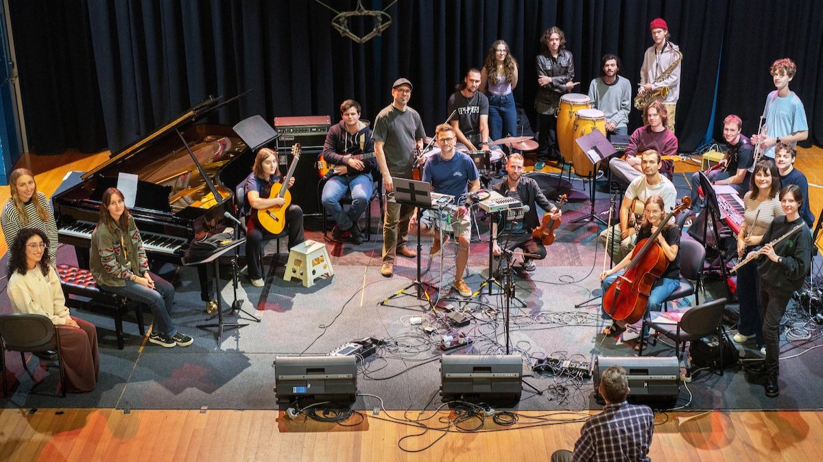 Large student ensemble performs on stage with mixed instruments during ANU School of Music folk collaboration.