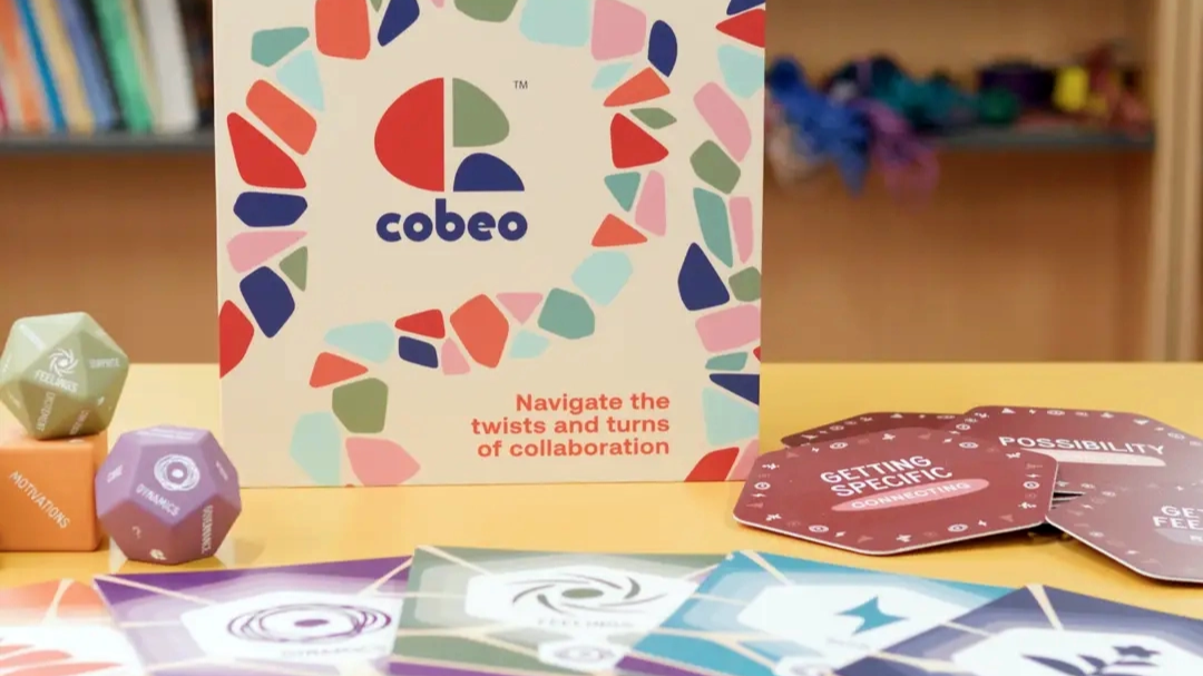 Cobee collaboration card game box with colourful design, cards and dice arranged on a table.