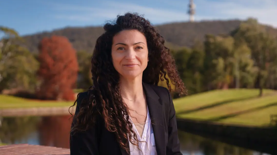 Portrait of Associate Professor Ana Sequeira in a blazer in front of Sullivan's Creek at ANU. 