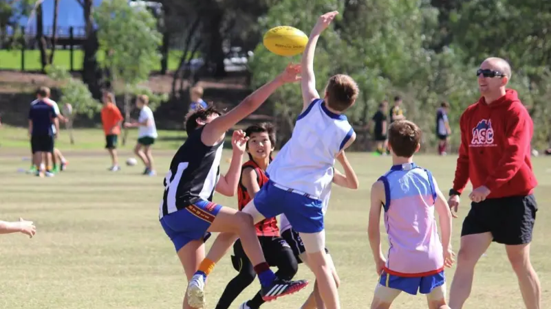 Children competing for a football during an outdoor game, with a coach nearby.