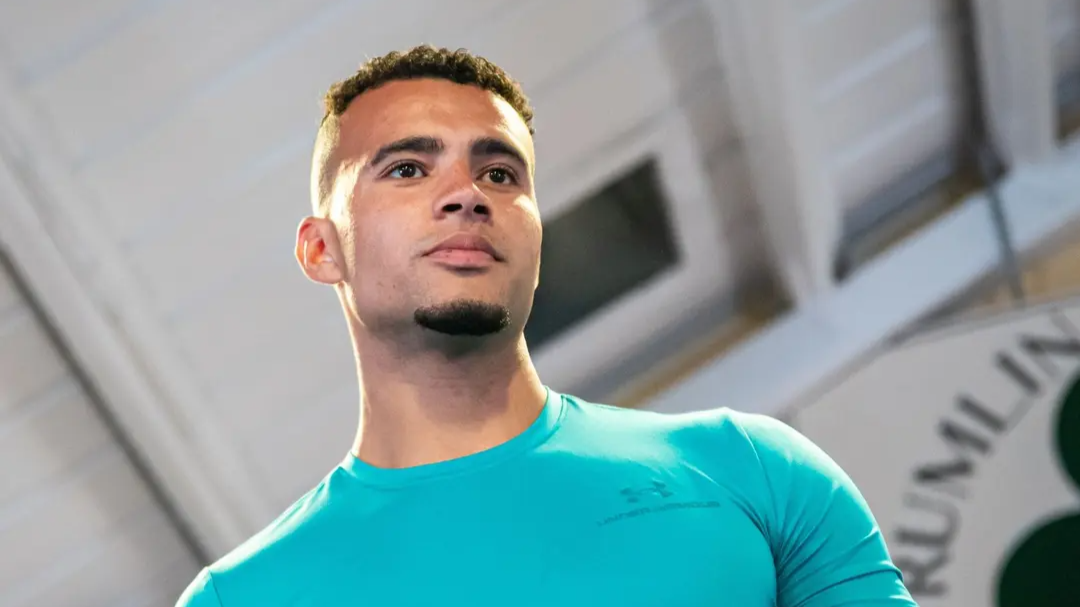 Low-angle portrait of a man in a teal athletic shirt looking ahead in an indoor setting.