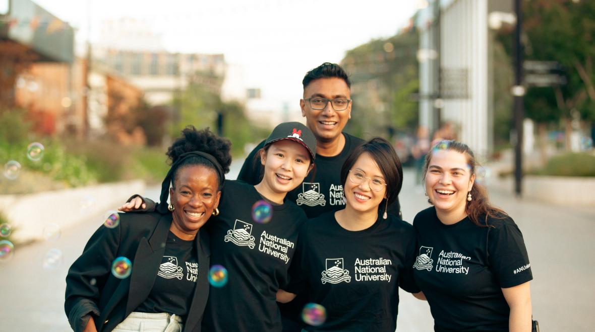 Five people wearing black ANU branded t-shirts and standing on University Avenue.   