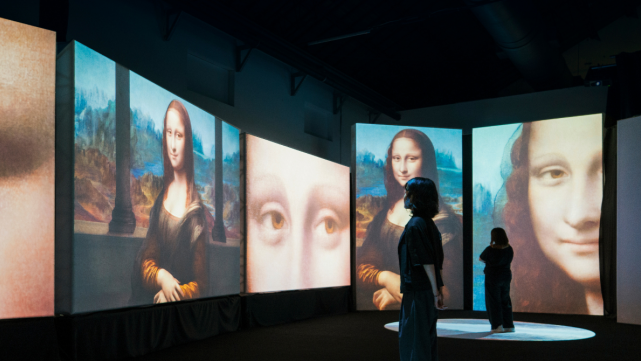 People viewing immersive Mona Lisa projections in a dark exhibition space.