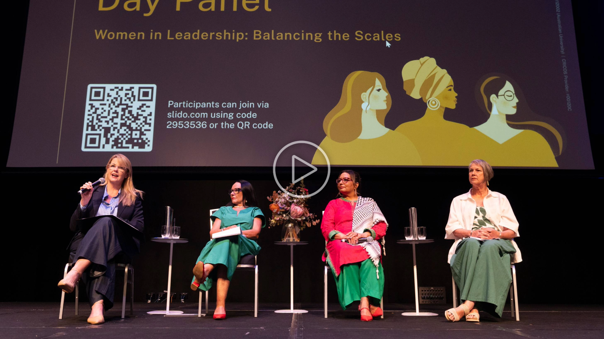 Four women sit on stage during an ANU International Women&rsquo;s Day panel discussion titled Women in Leadership: Balancing the Scales, with a presentation screen behind them and Interim Vice-Chancellor Rebekah Brown addressing the audience with a microphone.