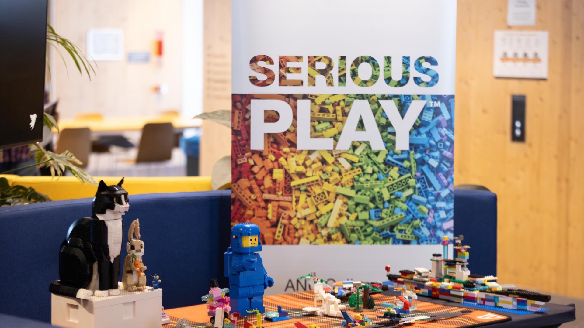 'Serious Play' banner with ANU branding and a cat, rabbit and man made out of Lego on the table in front of the banner. 