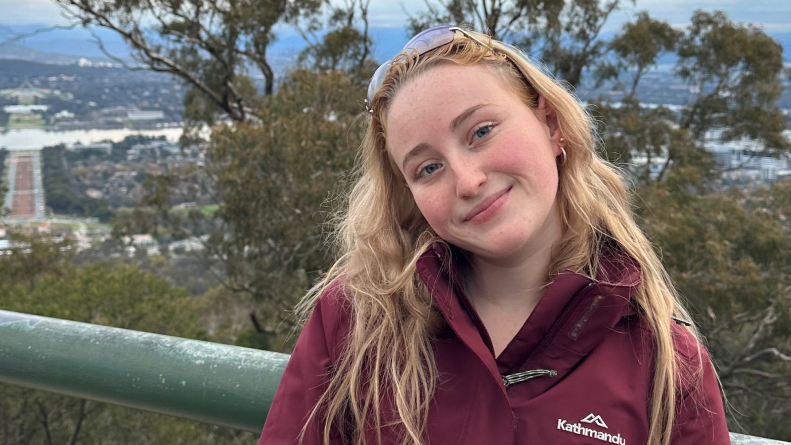 Lydianna Meade smiles at the camera from a lookout on Mount Ainslie, with Canberra and the Australian War Memorial visible in the background.