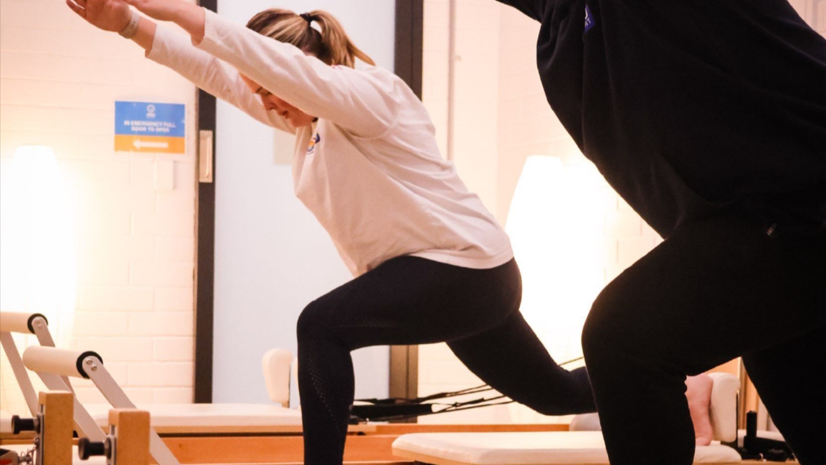 Participants performing reformer Pilates exercises in an indoor studio.