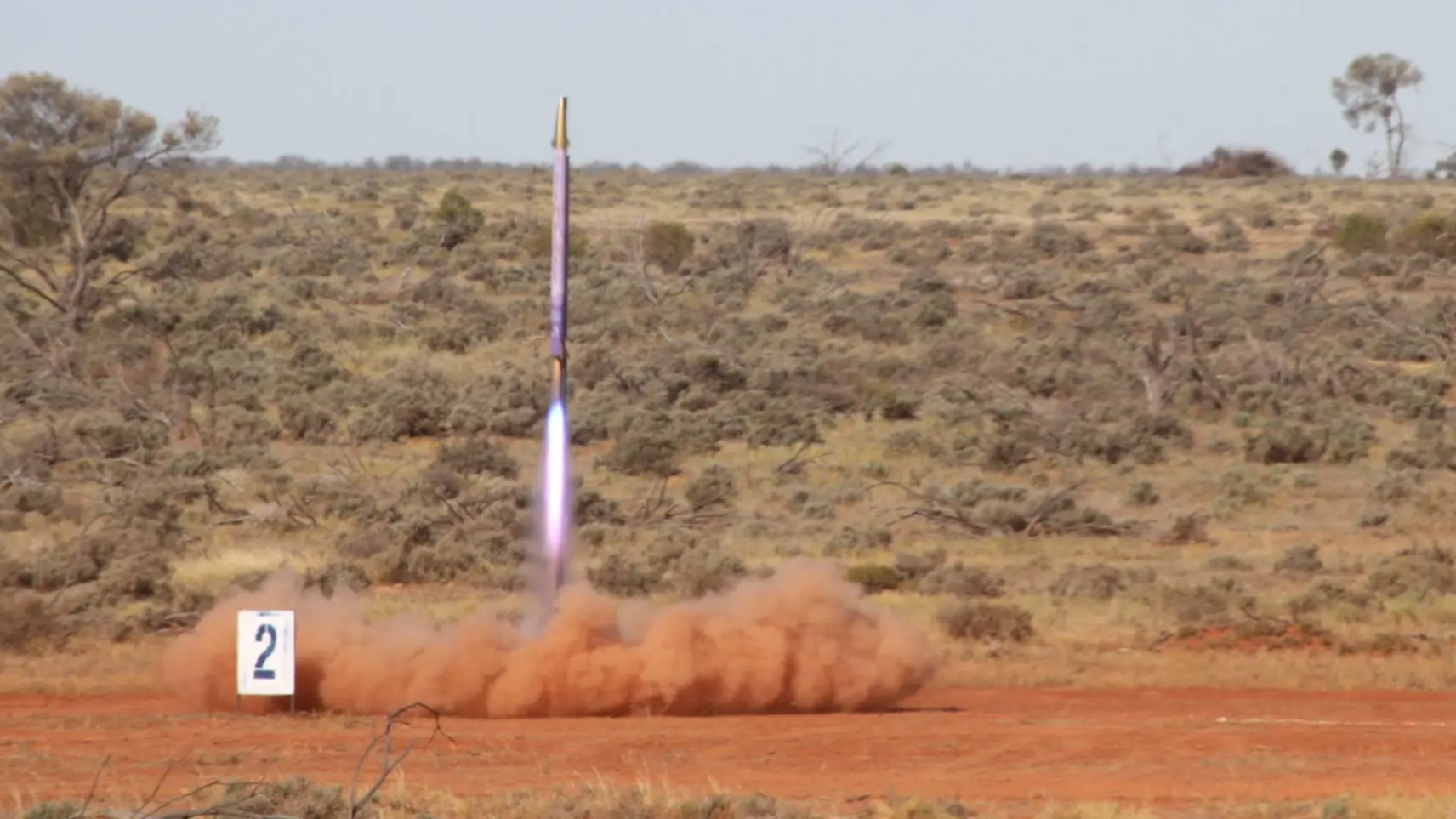 The ANU Rocketry built rocket &ldquo;Tempest&rdquo; lifts off above a cloud of dust at the outdoor launch site.