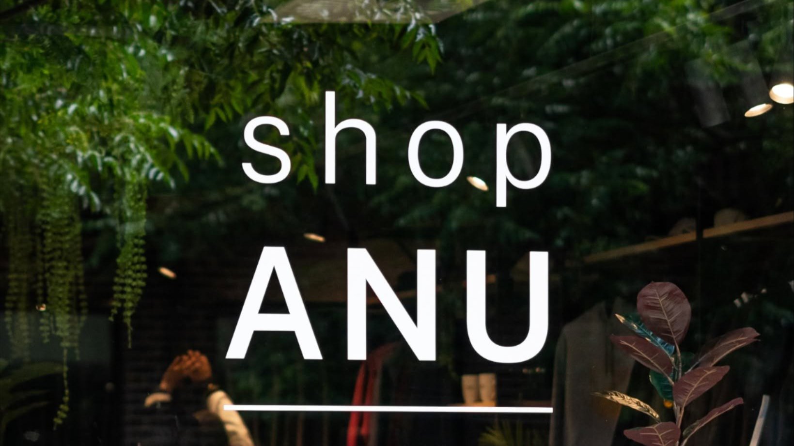 Shop ANU signage displayed on a glass storefront surrounded by indoor plants.