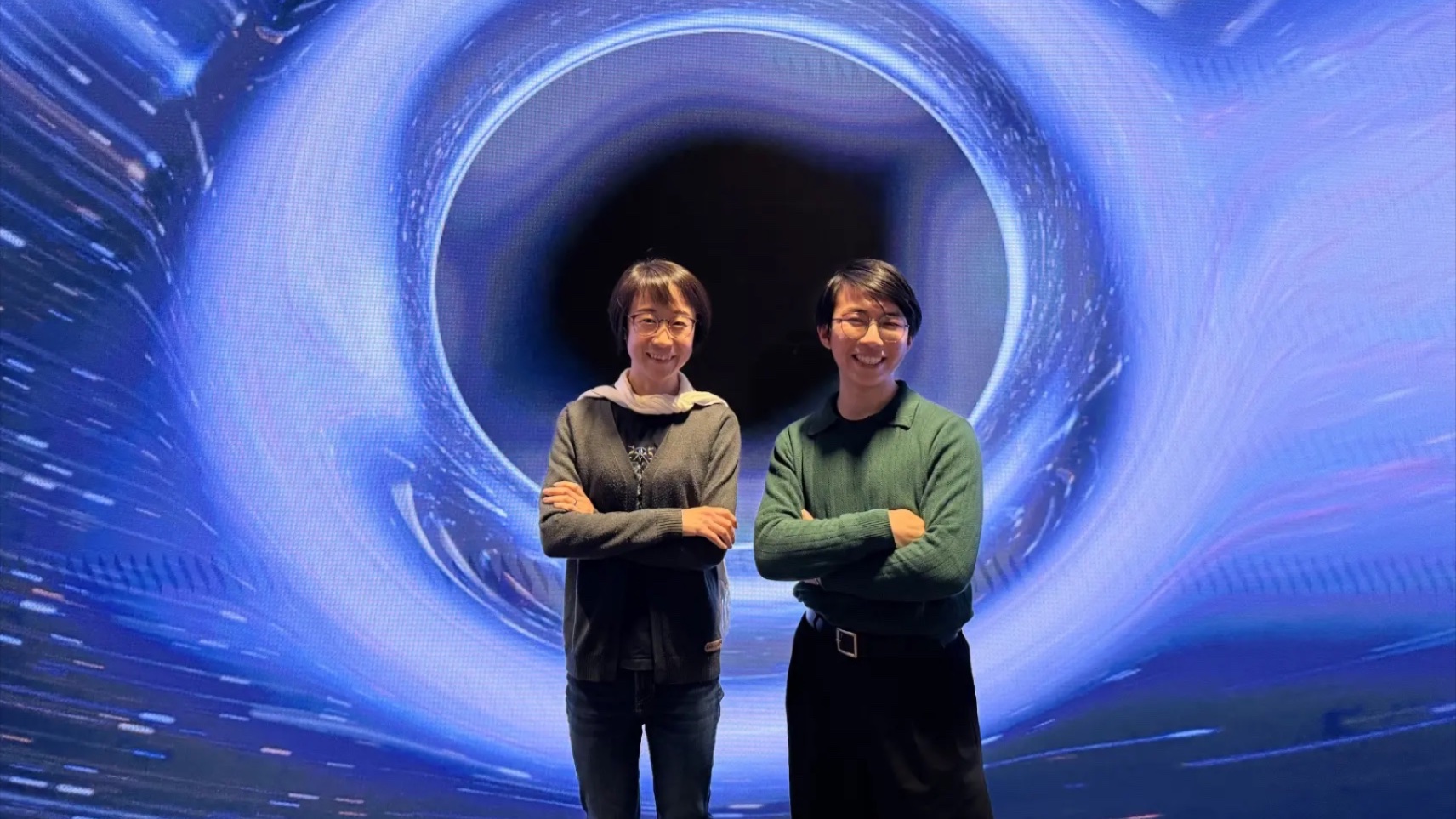  Dr Ling Sun and PhD candidate, Mr Neil Lu standing in front of a background that is meant to look like a black hole.