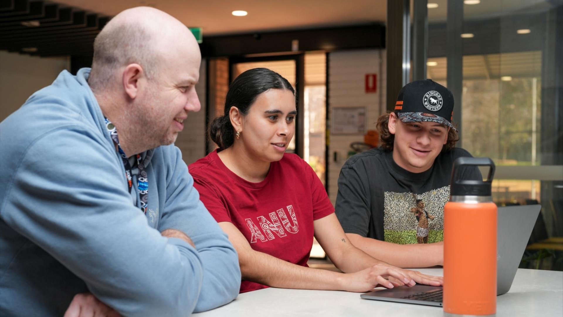 Three people sitting together, looking at something on a laptop. 