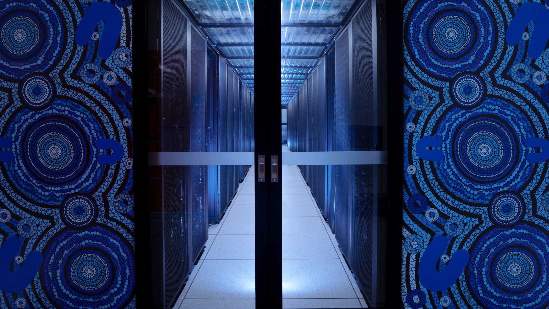 Rows of servers inside the Gadi supercomputer, framed by blue panels featuring artwork by Ngunnawal artist Lynnice Church.