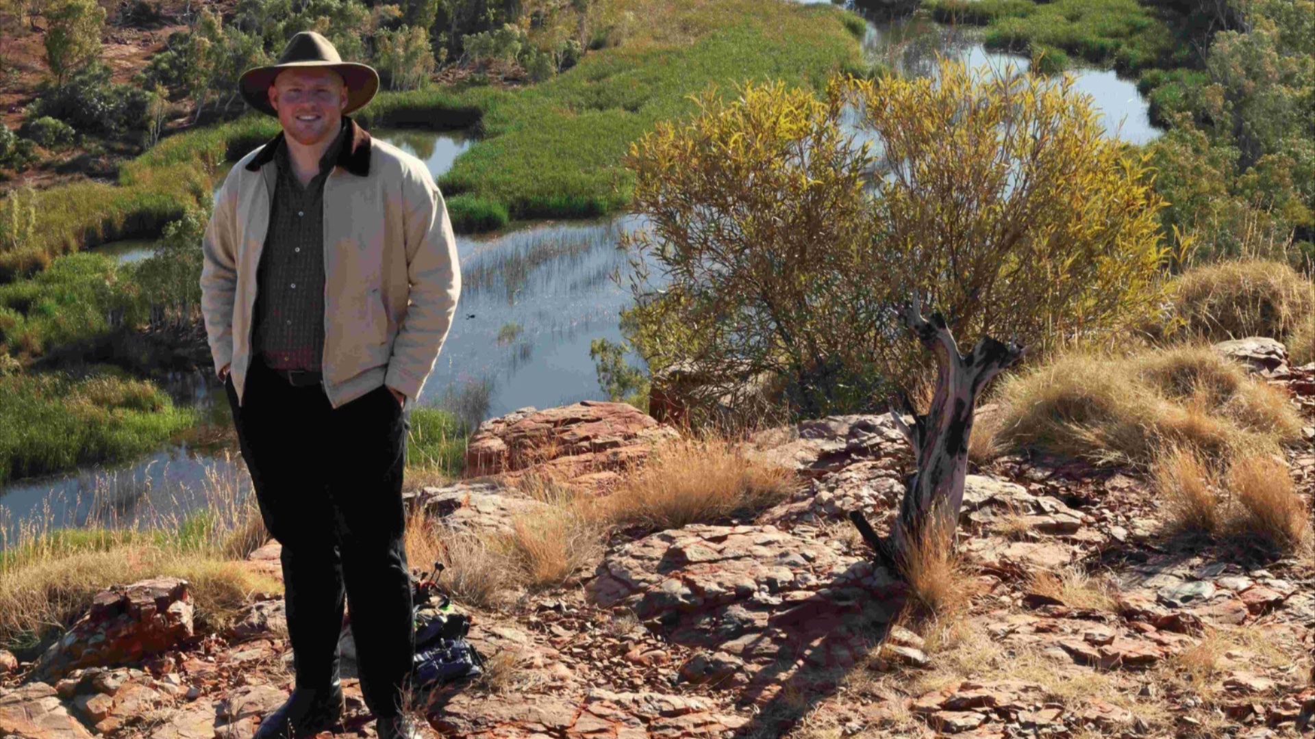 Noah Beford standing on a hilltop in front of a creek.  