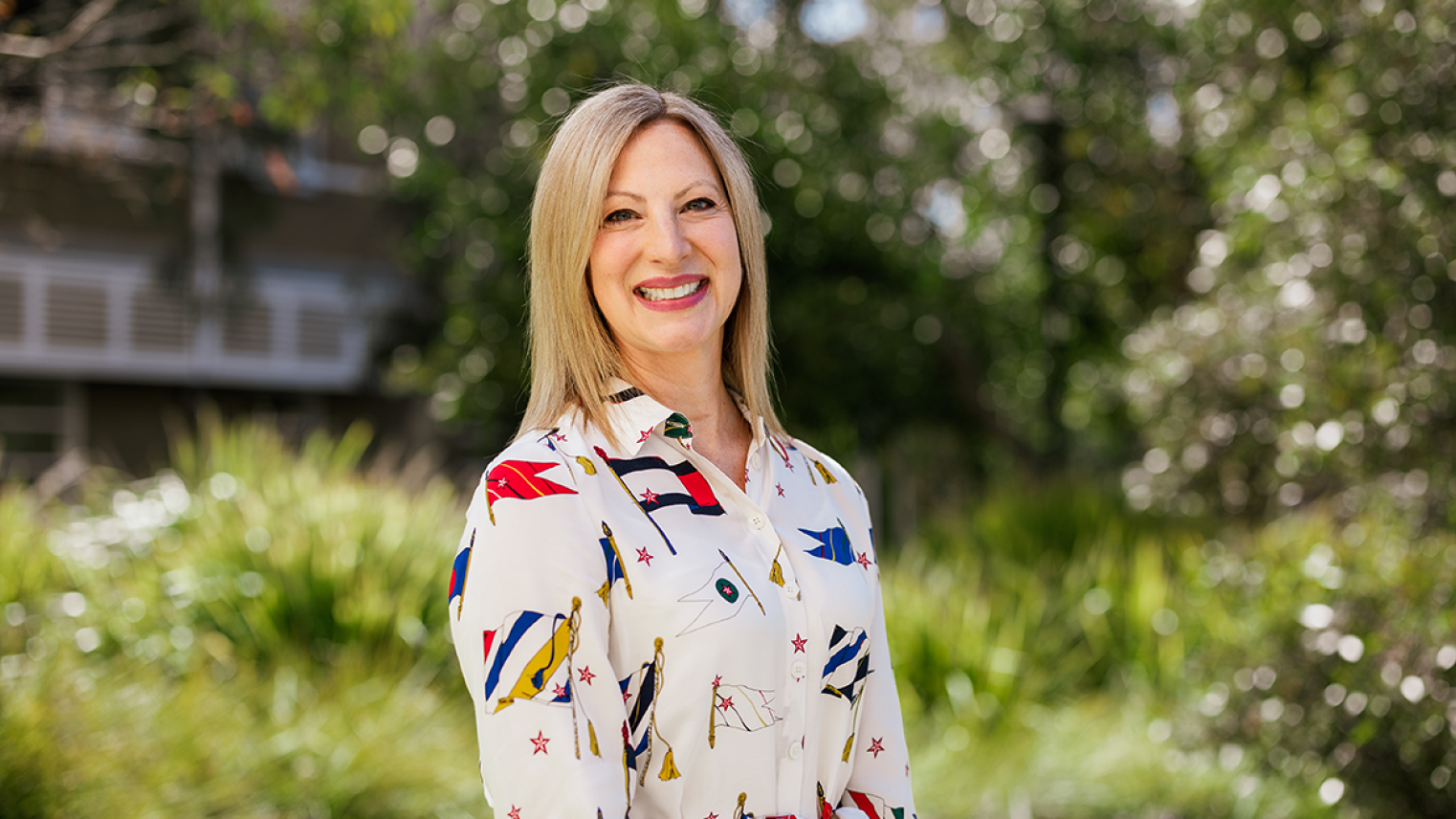 Smiling woman standing outdoors in a leafy garden.
