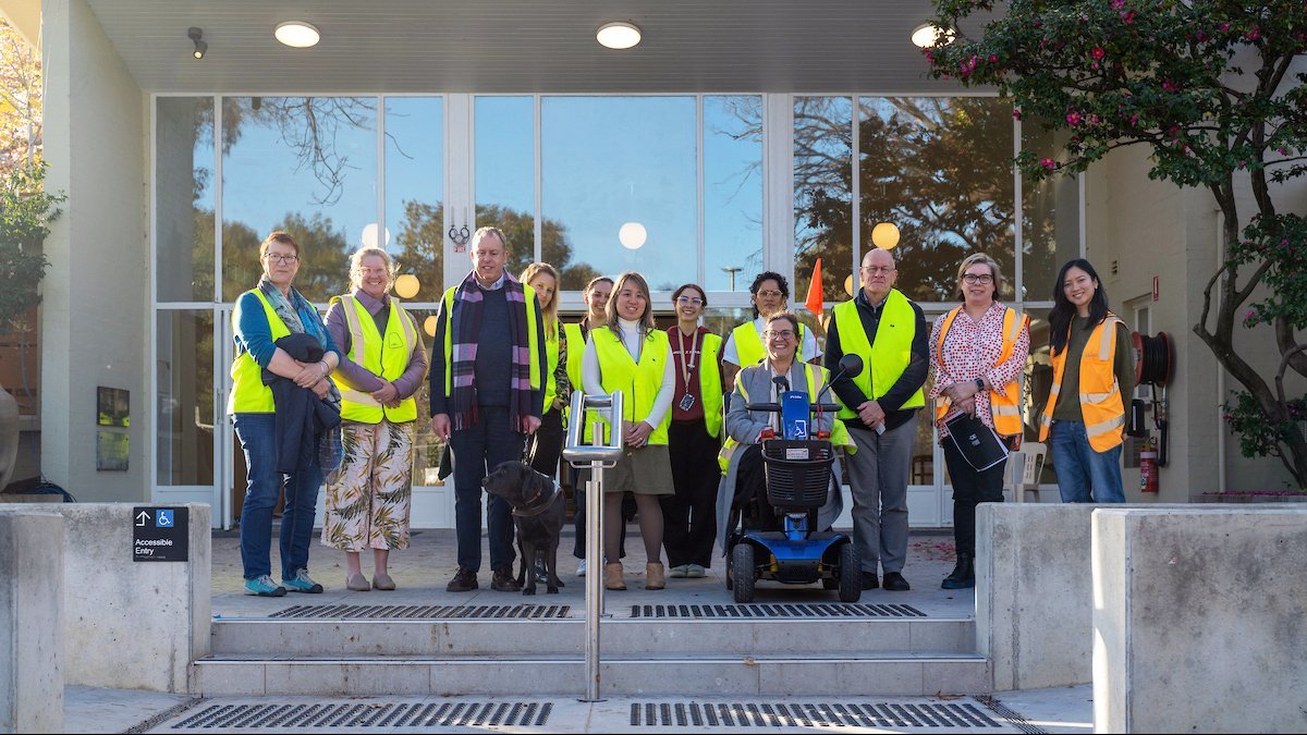 University staff wearing high-visibility vests gather outside University House during an accessibility awareness activity.