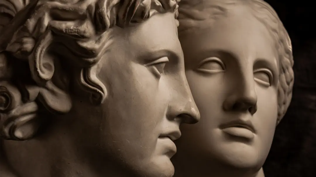 Close-up of two classical marble statues, their faces positioned close together as if sharing a secret.