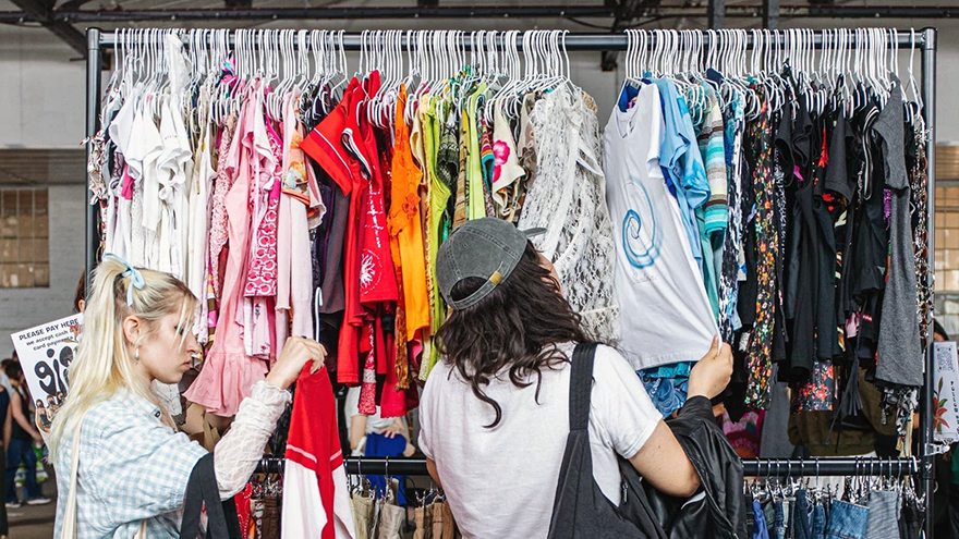 Picture of a Fashion Thrift Society event with two people browsing colorful garments on display. 