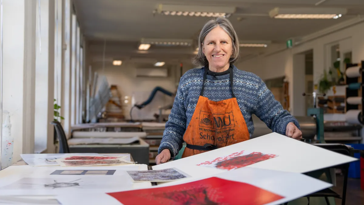 Dr Susanne Ilschner smiles while holding one of her artworks in an ������ƵSchool of Art printmaking studio.